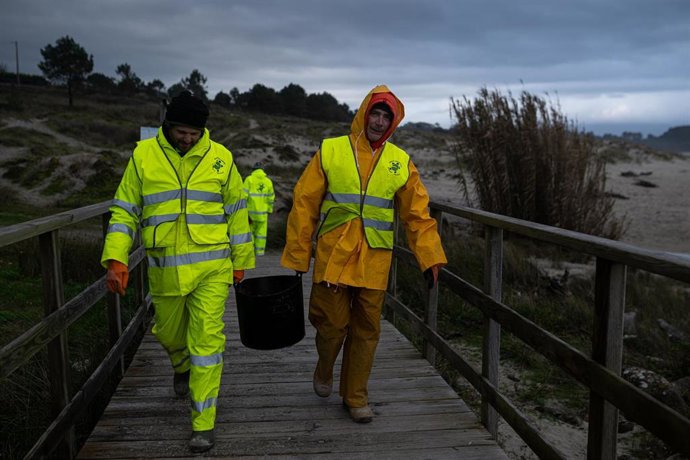 Dos hombres cargan un cubo lleno de pellets, en la playa Area Maior.