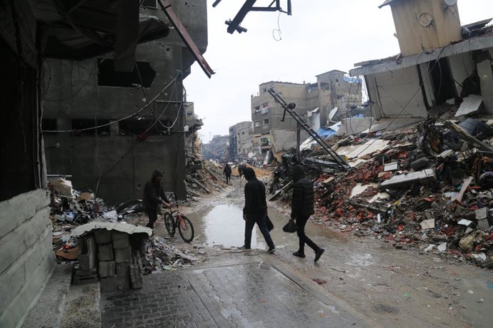 GAZA, Jan. 11, 2024  -- People walk past damaged buildings in the northern Gaza Strip town of Beit Lahia, on Jan. 11, 2024. The Palestinian death toll from ongoing Israeli attacks on the Gaza Strip has risen to 23,469, the Gaza-based Health Ministry sai