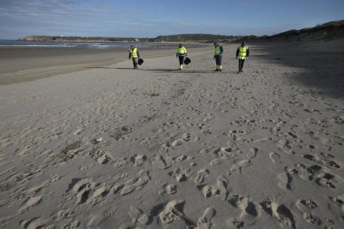 Archivo - Varios hombres recogen pélets en la playa