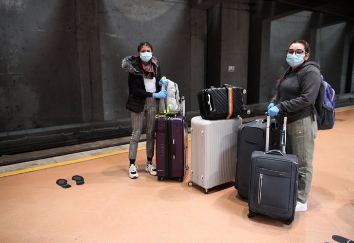 Archivo - Dos jóvenes cargadas con maletas esperan en uno de los andenes de Cercanías de Atocha para coger un tren con dirección al aeropuerto para volver su país de origen, México, en Madrid (España), a 14 de abril de 2020.