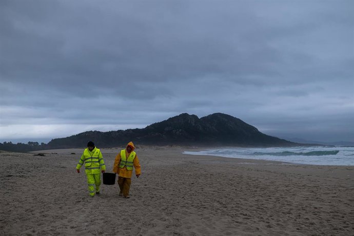 Dos hombres cargan un cubo lleno de pellets, en la playa Area Maior, a 13 de enero de 2024, en Muros, A Coruña, Galicia (España). La conocida ya como la marea blanca, se prevé que proceda de los seis contenedores del buque Toconao que cayeron al mar e