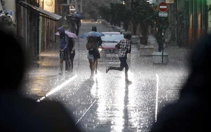 Archivo - Varias personas caminan bajo la lluvia, en València