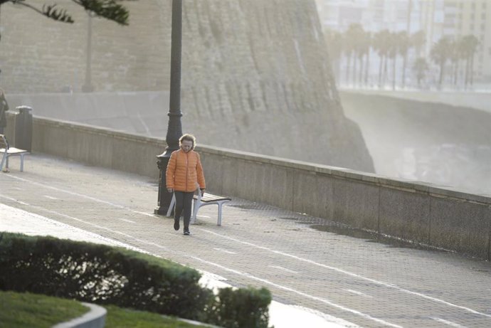 Una mujer pasea abrigada por Cádiz.
