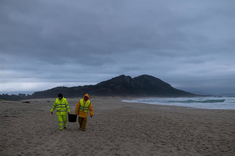 Dos hombres cargan un cubo lleno de pellets, en la playa Area Maior.