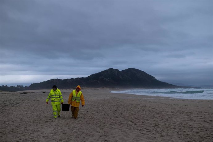 Dos hombres cargan un cubo lleno de pellets, en la playa Area Maior, a 13 de enero de 2024, en Muros, A Coruña, Galicia.