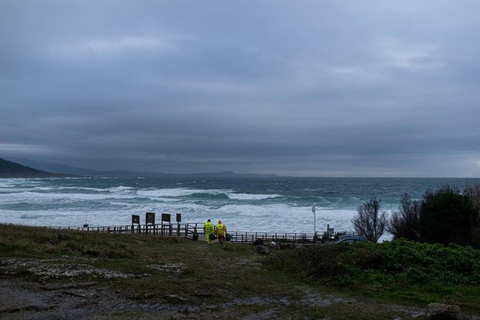 Dos hombres cargan un cubo lleno de pellets, en la playa Area Maior, a 13 de enero de 2024, en Muros, A Coruña, Galicia.