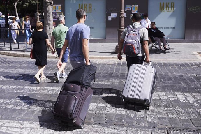 Archivo - Dos turistas, con maletas, cruzan un paso de peatones