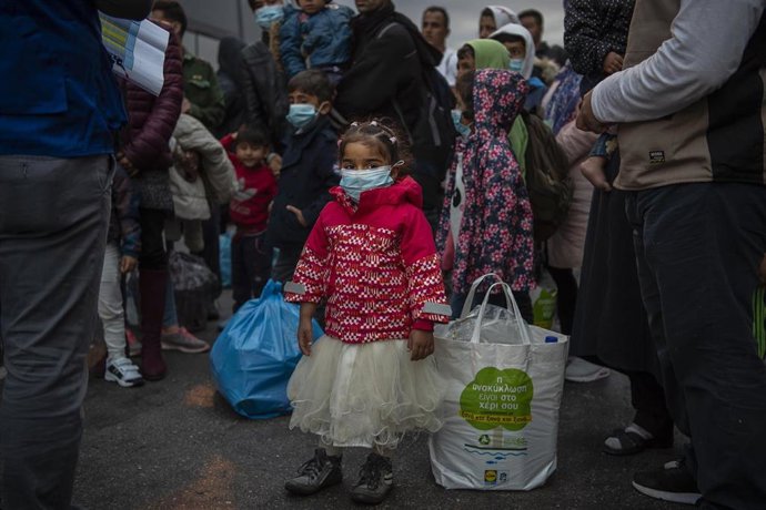 Archivo - Una niña con mascarilla, parte de un grupo de migrantes y refugiados que esperan a coger un autobús en el puerto del Pireo, en Grecia (archivo)