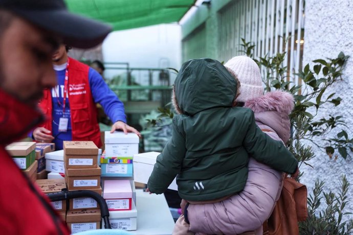 Archivo - Una mujer con un niño en brazos recibe ropa de invierno y zapatos que la Fundación Madrina entrega a familias en riesgo de vulnerabilidad en la sede de la Fundación Madrina.