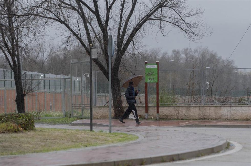 Un migrante se protege de la lluvia con un paraguas en las inmediaciones del centro de Emergencia, Acogida y Derivación en el Acuartelamiento 'Primo de Rivera'en Alcalá de Henares.