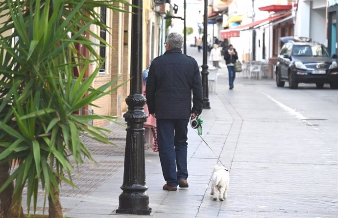 Un vecino pasea a su mascota por una calle de Tomares.