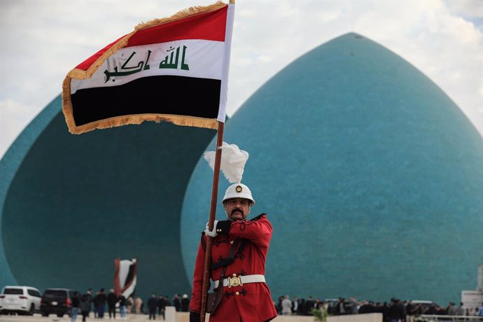 FILED - 22 January 2024, Iraq, Baghdad: A soldier holds the Iraqi flag as the remains of 41 Yazidis, who were found in a mass grave in the Sinjar district, are transported during a funeral ceremony at the Martyr's Monument in Baghdad. ISIS killed them dur