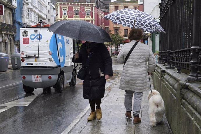 Dos personas se refugian del viento con paraguas en A Coruña.