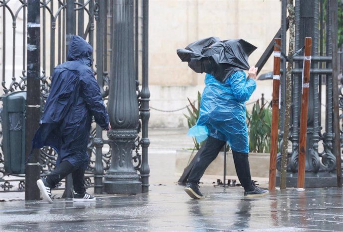 Dos pesonas caminan bajo la lluvia junto al Rectorado.