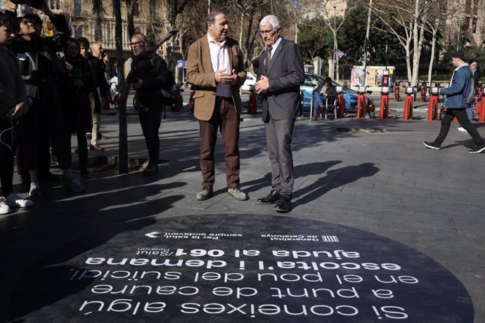 El conseller de Salud, Manel Balcells, y el coordinador del PLAPRESC (Plan de prevención del suicidio de Catalunya), Diego Palau, hablan delante de uno de los vinilos de la campaña 'No el deixis caure en el pou', ubicado en la Plaza Univesitat (Barcelona)