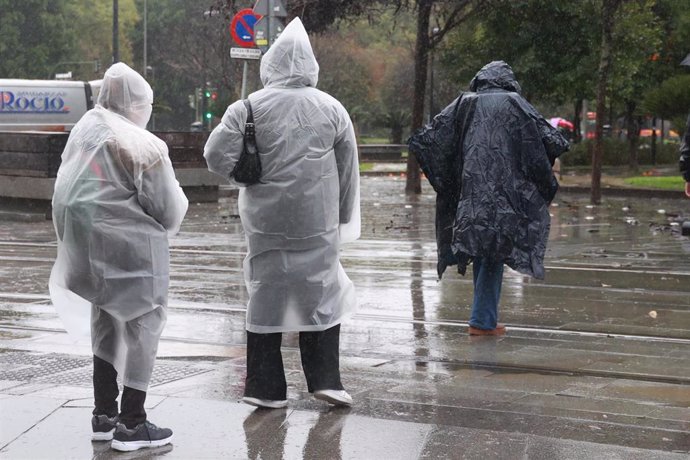 Varias personas se protegen de la lluvia con impermeables en Sevilla