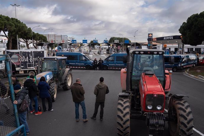 Agentes de Mossos d'Esquadra delante de los agricultores y tractores que han cortado uno de los accesos a Mercabarna, a 13 de febrero de 2024, en Barcelona