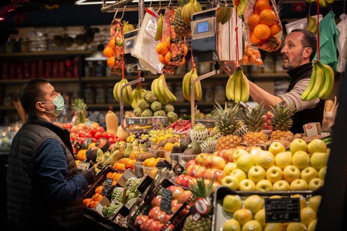 Archivo - Un hombre protegido con mascarilla es atendido en una frutería durante el segundo día laborable del estado de alarma por el coronavirus, en Barcelona (España), a 17 de marzo de 2020.