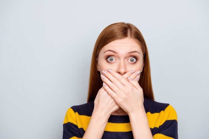 Archivo - Hush scared business people coughing big pop-eyed fashion concept. Close up portrait of pretty cute terrified frightened mute dumb silent manager model with palms over mouth isolated gray background