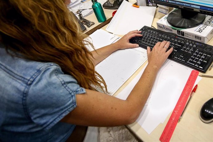 Archivo - Una mujer escribe en el teclado de su ordenador, con papeles alrededor mientras trabaja en la oficina. 
