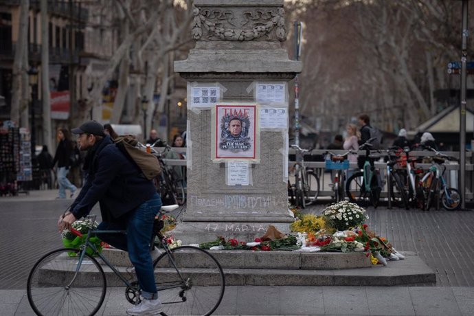 Una persona pasa junto a un homenaje a Alexéi Navalni a los pies de la farola modernista junto a la plaza Catalunya, en La Rambla de Barcelona