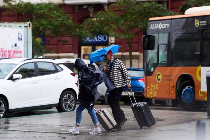 Archivo - Varias personas se cubren de la lluvia y el viento con paraguas, en Santander