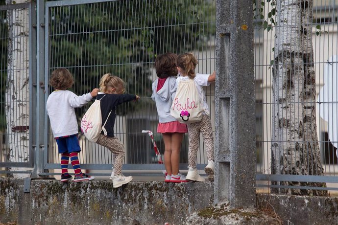 Archivo - Varios niños y niñas se encaraman a la valla de un colegio