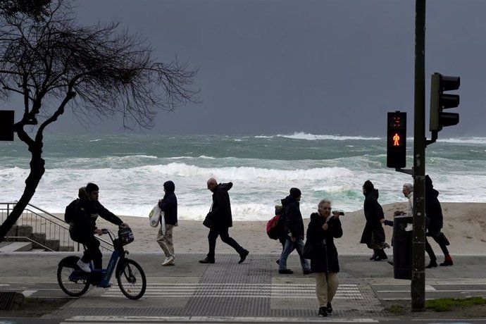 Varias personas caminan delante de las olas durante el frente meteorológico, a 23 de febrero de 2024, en A Coruña, Galicia (España). La Agencia Estatal de Meteorología (Aemet) decretó un aviso naranja por temporal costero en el litoral gallego que ya está