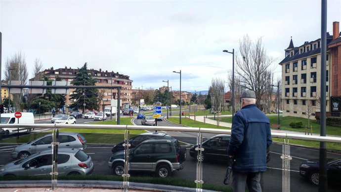 Un pensionista observa el tráfico en la glorieta de la Cruz Roja de Oviedo, con la iglesia de San Julián de los Prados al fondo.