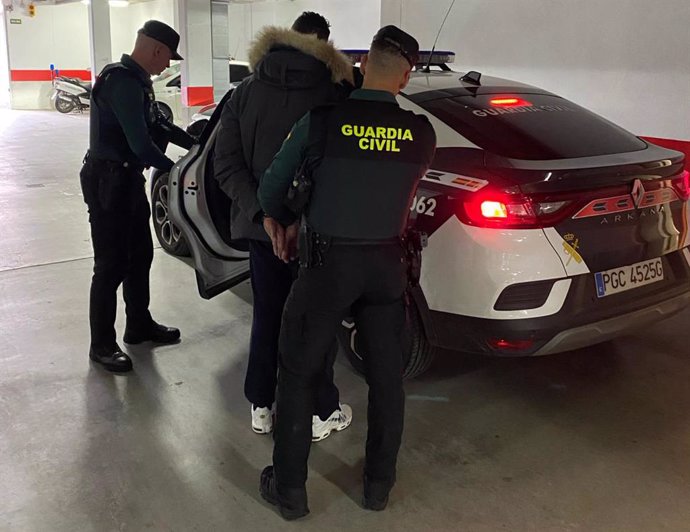 Agentes de la Guardia Civil introducen en el coche a uno de los detenidos por el robo de un reloj de alta gama.