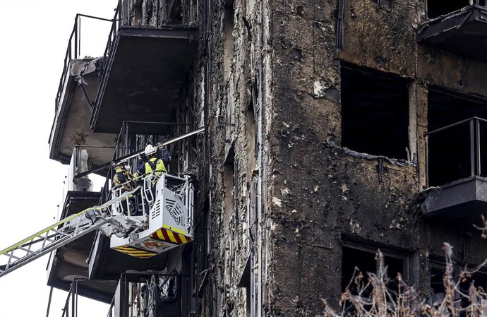 Bomberos en una grúa sanean la fachada quemada en Campanar