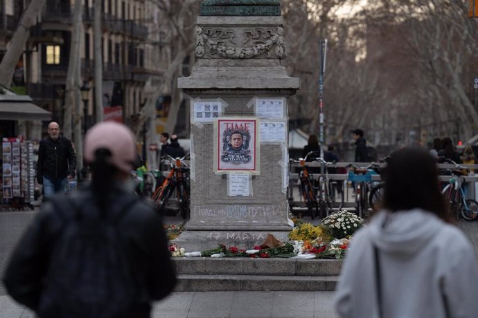 Varias personas observan las velas, flores y fotos en homenaje a Alexéi Navalni a los pies de la farola modernista junto a la plaza Catalunya, en La Rambla de Barcelona