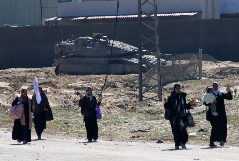 05 March 2024, Palestinian Territories, Khan Yunis: Displaced Palestinian women carrying their belongings walk past Israeli forces while fleeing the Hamad City area in Khan Yunis in the southern Gaza Strip.