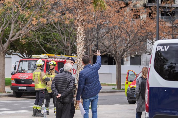 Bombers amb alguns dels afectats de l'incendi de l'edifici, als voltants de l'immoble, al barri de Campanar