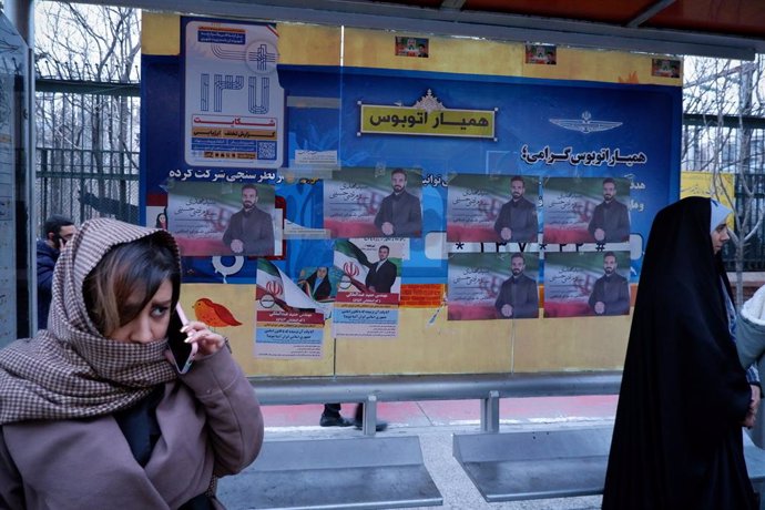 Mujeres en una parada de autobús de Teherán con carteles electorales de candidatos a las elecciones legislativas en Irán