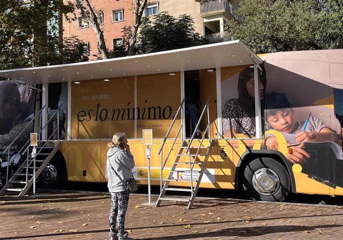 Archivo - Una mujer habla por teléfono delante del autobús del Ingreso Mínimo Vital