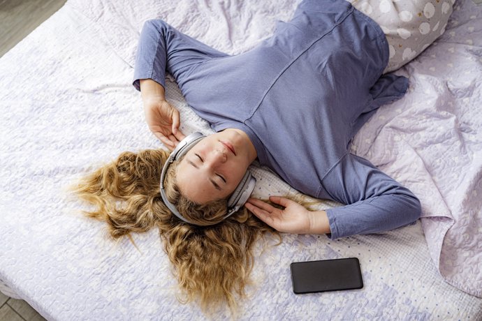 Chica adolescente con los ojos cerrados pasando el tiempo escuchando música acostada en su cama