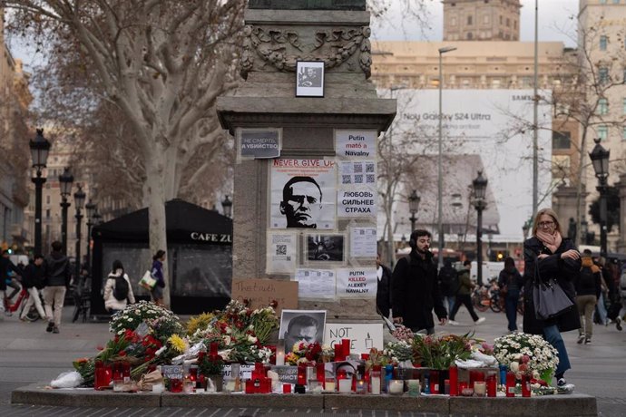 Una persona observa las velas, flores y fotos en homenaje a Alexéi Navalni a los pies de la farola modernista junto a la plaza Catalunya, en La Rambla de Barcelona