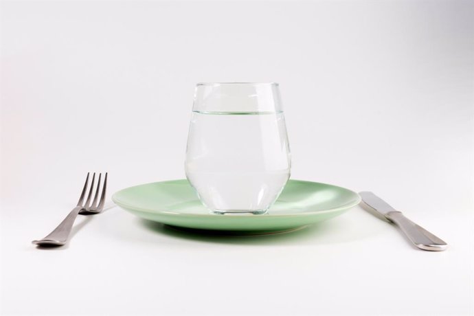 Archivo - Vaso de agua en un plato con cuchillo y tenedor aislado sobre fondo blanco