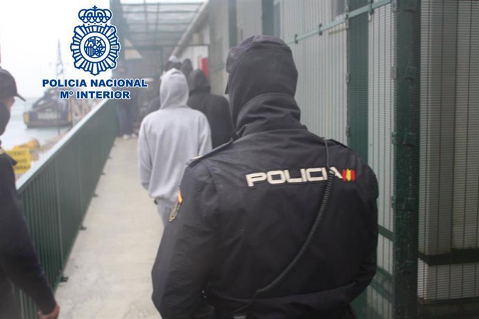 Archivo - Un agente de Policía Nacional custodia a uno de los presuntos patrones de patera.