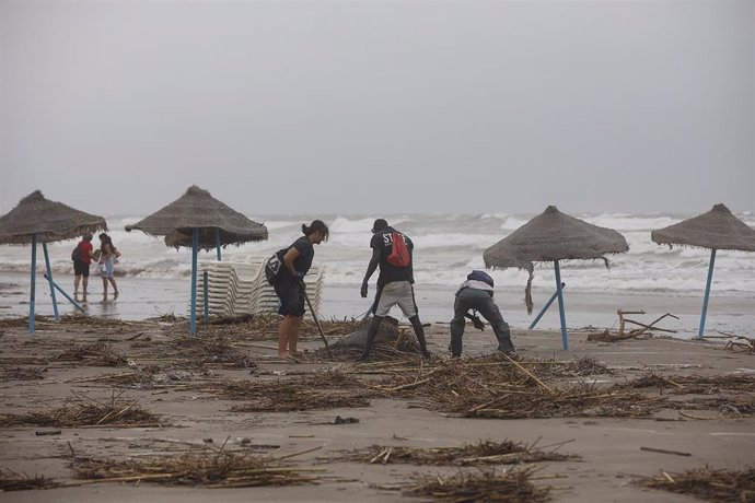 Archivo - Varias personas tratan de colocar una sombrilla caída por los fuertes vientos que ha provocado la DANA en la playa de la Malvarroasa, en imagen de archivo