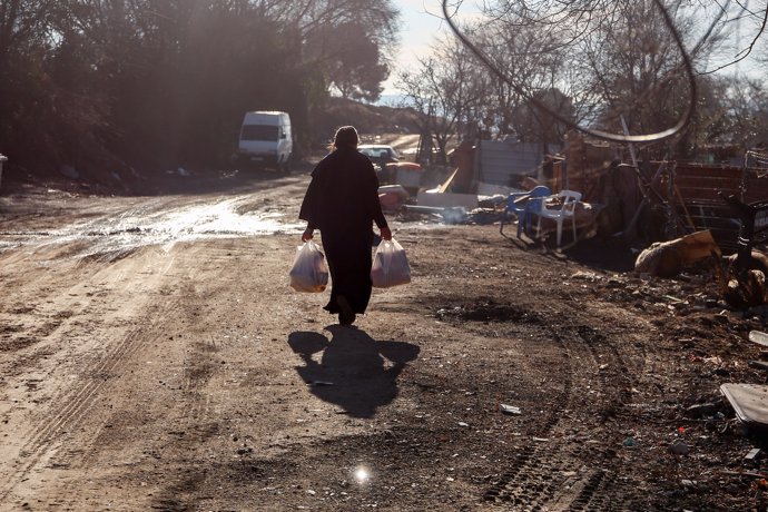 Una mujer camina con bolsas que ha recogido en la entrega de regalos y alimentos organizada por la Fundación Madrina, en la Cañada Real, a 31 de diciembre de 2021, en Madrid, (España).