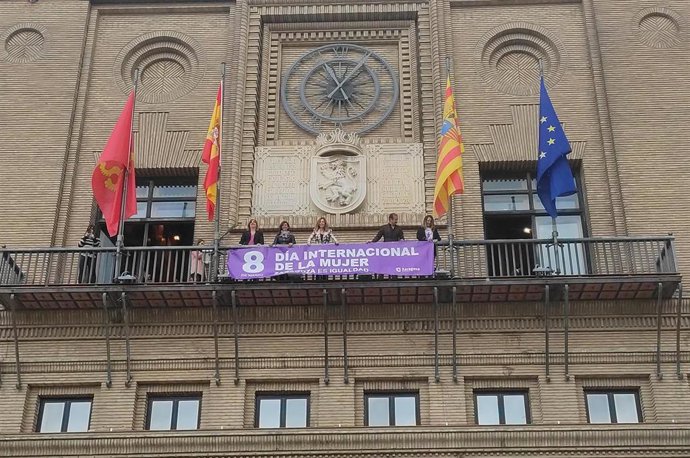 La alcaldesa de Zaragoza, Natalia Chueca, coloca la pancarta del 8M en la Casa Consistorial junto a los portavoces de PSOE, PP y ZeC, así como la consejera municipal de Políticas Sociales, Marian Orós.