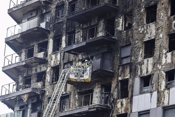 Bomberos en una grúa sanean la fachada quemada de uno de los bloques de Campanar