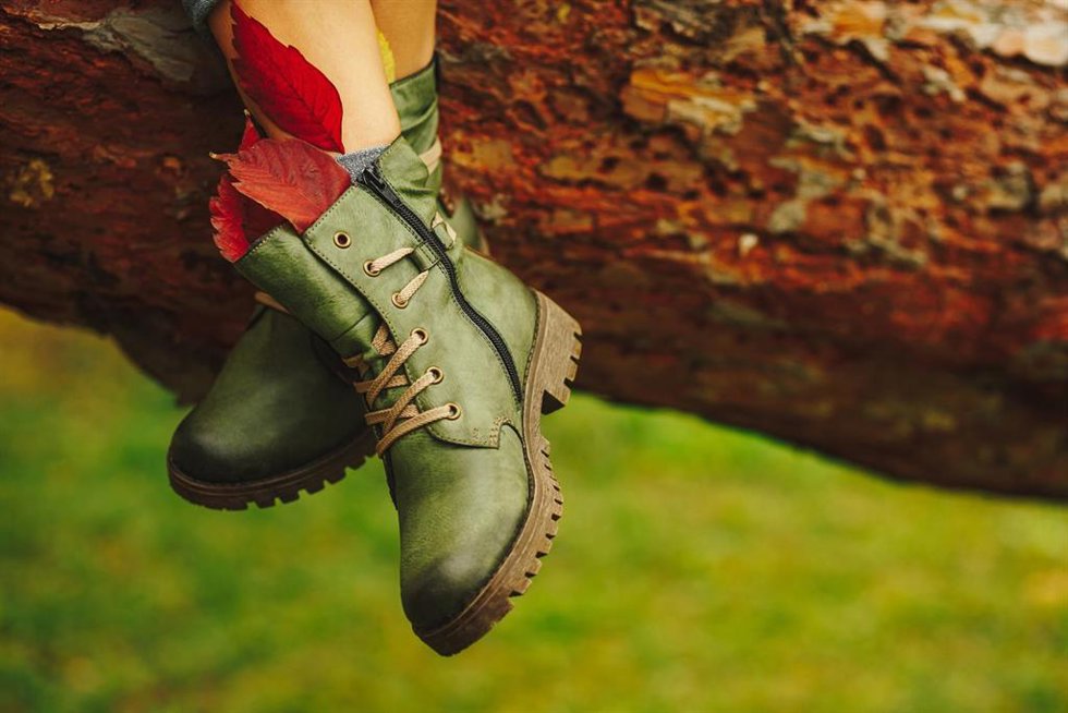 Archivo - Green leather boots on women legs decorated with fall autumn foliage leaves on brown tree background. Design, Shoes concept, advertising.