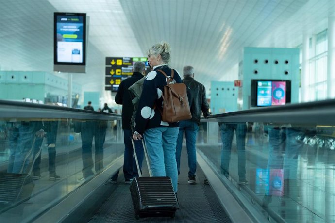 Archivo - Una mujer camina con su maleta en una cinta en el aeropuerto de El Prat