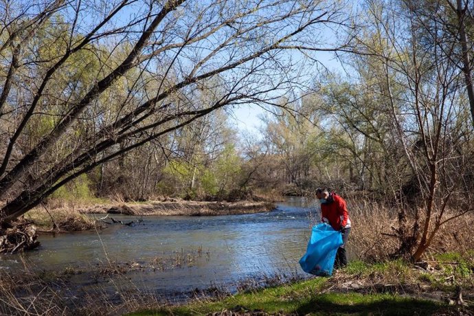 Un voluntario retira basuraleza en un río.