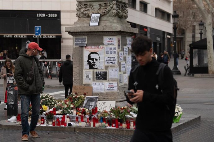 Una persona observa las velas, flores y fotos en homenaje a Alexéi Navalni a los pies de la farola modernista junto a la plaza Catalunya, en La Rambla de Barcelona, a 22 de febrero de 2024