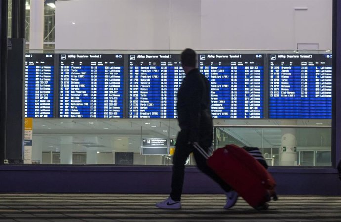 13 March 2024, Bavaria, Munich: A man with a suitcase walks past a display board for departures at Munich Airport. 