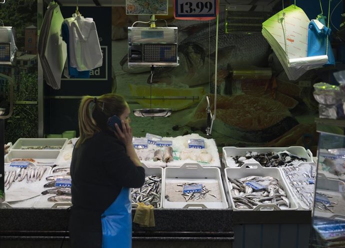 Archivo - Una pescadera atiende el teléfono móvil en un puesto de un mercado, a 15 de marzo de 2023, en Madrid (España). 